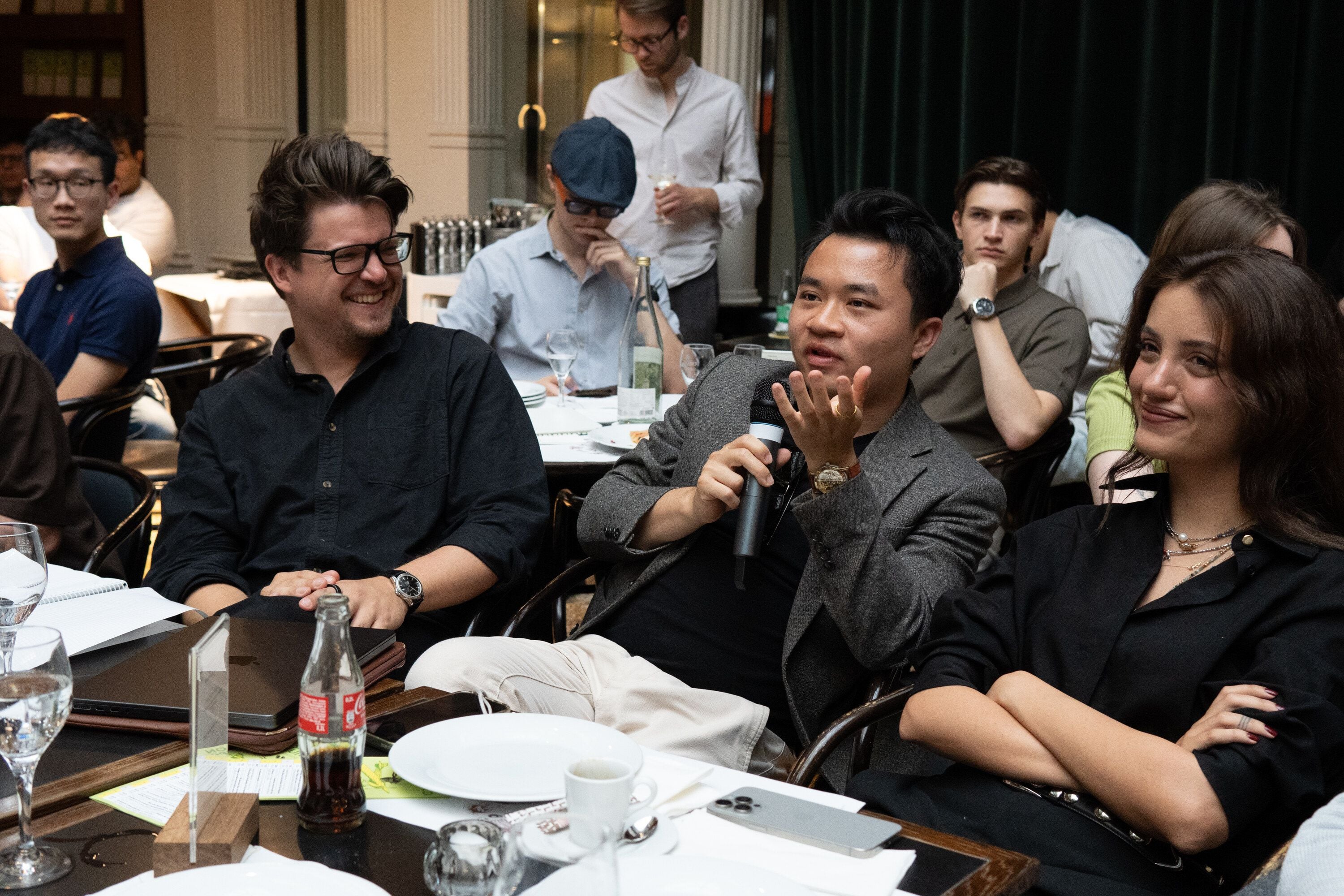 A participant asks a question into a microphone at a dinner table during the ELAB Midterm Pitch